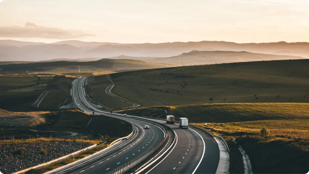 Scenic highway with trucks and car through rolling hills at golden hour—Grey Cap service locations across regional routes.