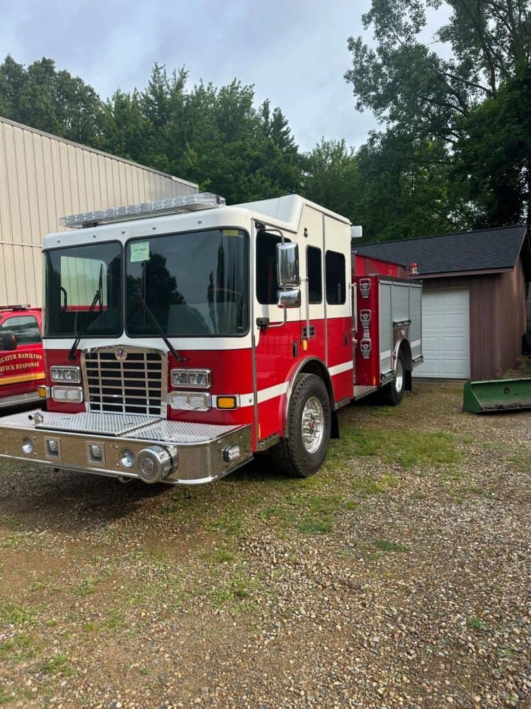 Red and white fire truck on gravel beside bigger trailer truck —Grey Cap emergency equipment transport visual.