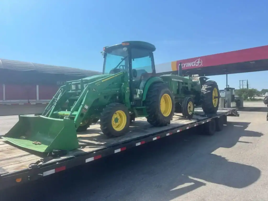 Green John Deere tractor with front loader secured on a Grey Cap flatbed trailer for equipment transport.