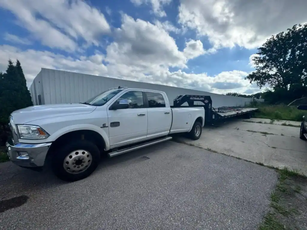 White Grey Cap dually pickup truck with a heavy-duty flatbed trailer for equipment delivery service.