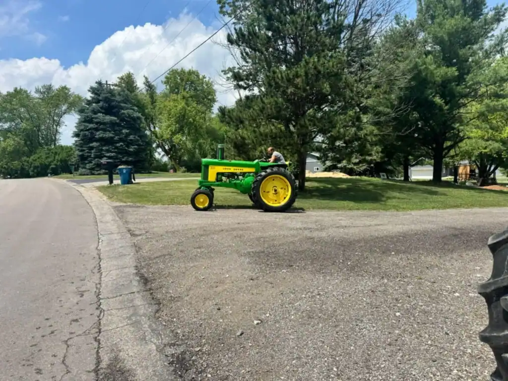 John Deere tractor in operation near a residential area, representing Grey Cap Transportation’s trusted partnership with industry leader John Deere for delivery services across Indiana and Michigan.
