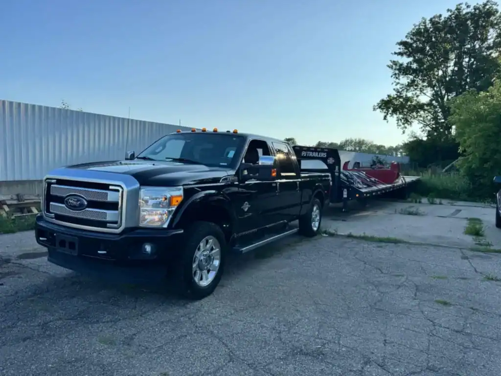 Black Ford pickup truck towing a PJ Trailers flatbed loaded with red industrial equipment, part of Grey Cap Transportation’s delivery fleet operating across Indiana and Michigan.