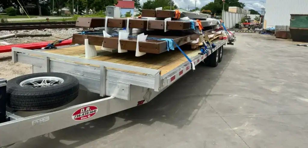 Flatbed trailer loaded with metal beams and wrapped items—Construction Materials transport by Grey Cap for industrial delivery.