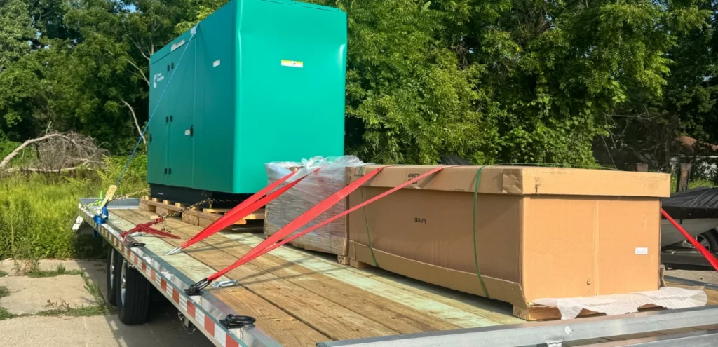 Flatbed trailer loaded with green industrial machine, boxes, and pallet—Expedited Shipping by Grey Cap.