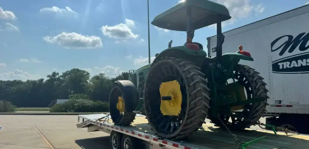 Green and yellow tractor secured on flatbed trailer—Farm Equipment transport by Grey Cap for agricultural delivery.