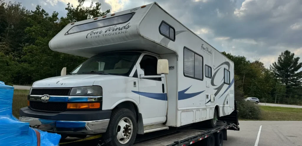 White RV labeled “Four Winds Five Thousand” on flatbed trailer—transported by Grey Cap at South Bend for relocation or delivery.